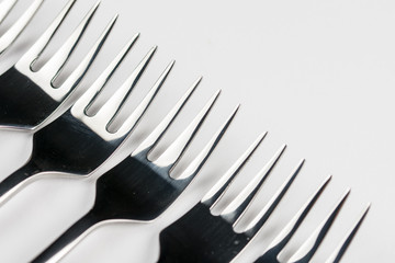 Selective focus closeup macro metal shiny forks lined up over white background