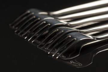 Metal shiny forks isolated over black reflective background with copy space