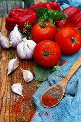 Organic fresh juicy summer vegetables lie on a wooden cutting board: tomatoes, paprika, garlic, herbs and spices in a wooden spoon