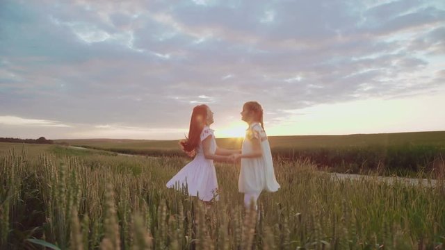 Two young girls in embroidery dress jumping in circle in the wheat and rejoicing