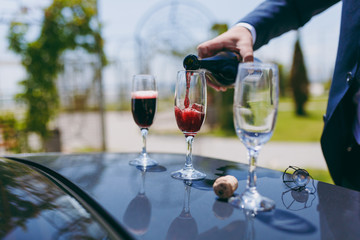 A man pours champagne into the crystal glasses on the hood of the car