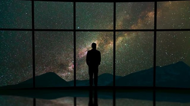 The man stand near a panoramic window on the starry sky background. time lapse