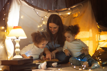 Reading and family games in children's tent. Mother and two twins daughters with books and...