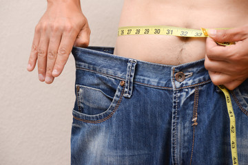 Concept of Man losing weight. Men wearing big jeans after diet.