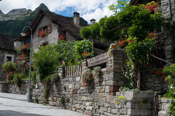 Fototapeta na wymiar Sonogno small town in the swiss mountains. Street with old stone houses decorated with flowers.