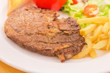 Close up grilled roast pork steak with french fries and vegetables and potatoes on white plate
