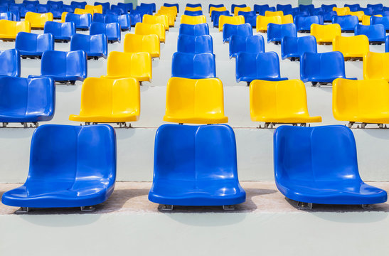 Rows of empty blue and yellow plastic seats in public sport stadium 