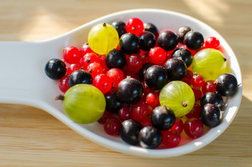 Naklejka na ściany i meble Fresh berries of a gooseberry, black and red currant in a white spoon on a wooden background.