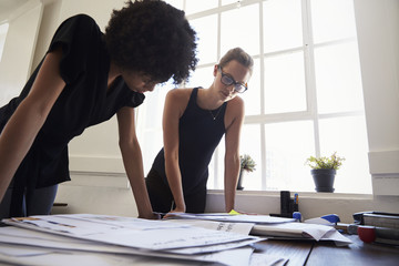 Two young businesswomen looking at documents in an office