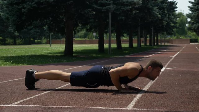 Athletic sportsman doing pushups on running track