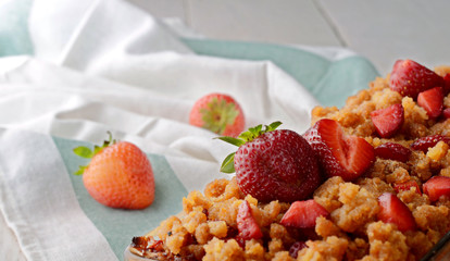 Baked granola with strawberries on a white wooden table