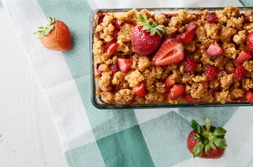 Baked granola with strawberries on a white wooden table