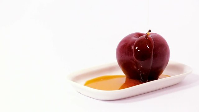 Cinemagraph of pouring honey on red apple on white plate
