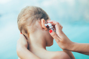 Mother treating little boy ear infection by the sea