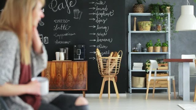 Woman talks on the phone in dining room with chalkboard and woodencommunal table