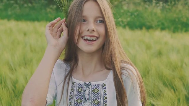 Cheerful young girl in embroidery dress posing with wheatears in a hand in field