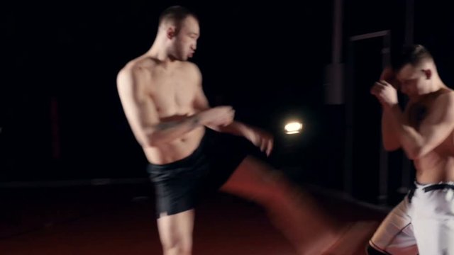 Two men spar in a dim boxing studio.  