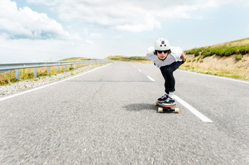 A guy wearing a helmet and sunglasses is riding his longboard on a country road