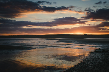 Obraz premium Sunset sky colours reflected in wet sand on beach at low tide,
