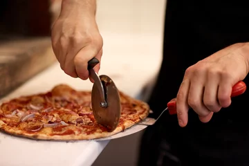 Selbstklebende Fototapeten cook hands cutting pizza to pieces at pizzeria © Syda Productions
