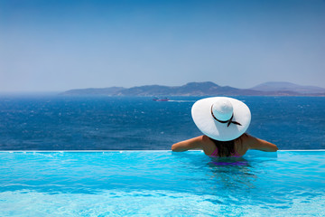 Fototapeta na wymiar Elegante Frau mit weißem Hut genießt die Aussicht von einem Pool auf das Meer