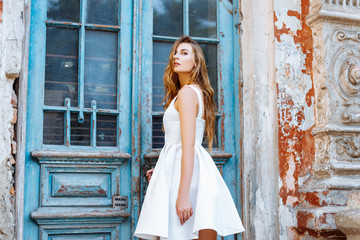 Naklejka premium Beautiful girl in a white dress near a blue door