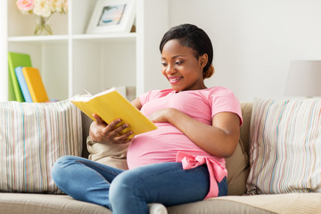 happy pregnant african woman reading book at home