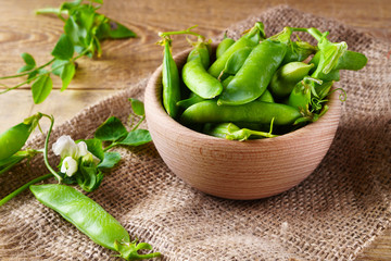 Fresh raw green peas beans  in light wooden bowl on canvas jute cloth vintage wooden background,  selective focus. Healthy eating antioxidant nutrition concept.