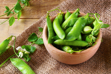 Fresh raw green peas beans  in light wooden bowl on canvas jute cloth vintage wooden background, horizontal, selective focus. Healthy eating antioxidant nutrition concept, top view.