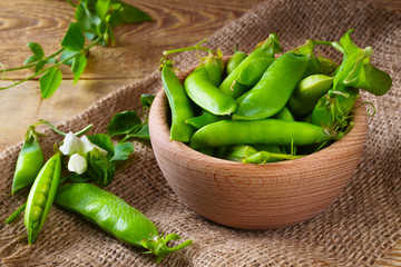 Fresh raw green peas beans  in light wooden bowl on canvas jute cloth rustic vintage wooden background, horizontal, selective focus. Healthy eating antioxidant nutrition concept.