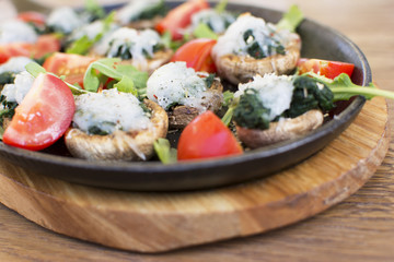 Cooked mushrooms filled with spinach and a touch of white topping. Tomatoes and green leafs on the side. Topping with the touch of green seasoning. Beautifully served plate at the restaurant.