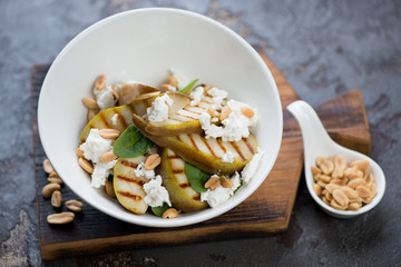 Salad with spinach, grilled pears, nuts and feta cheese in a white bowl on a wooden serving board, studio shot