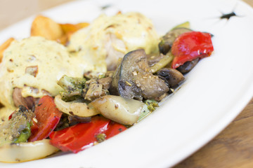 Roasted chicken breast rolls wrapped in bacon slices, served with fried potatoes and cooked vegetables. Topping with the touch of seasoning. Beautifully served plate at the restaurant.