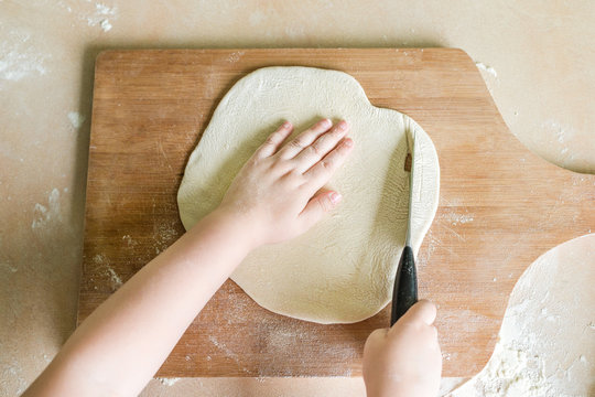 children's hands cutting raw rolled dough