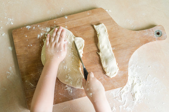 children's hands cutting raw rolled dough