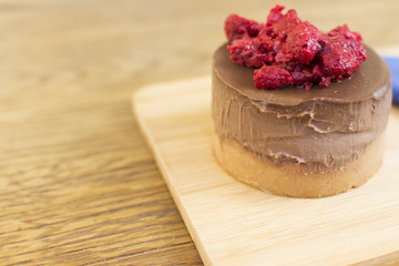 Piece of cake with chocolate glaze and raspberries on a plate on a wooden background. Blue napkin with a spoon beside the cake.