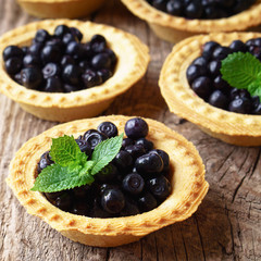 Bilberry, whortleberry or European blueberry with fresh green mint in mini tarts (tartlets) on rough rusric rural wooden table or background. Healthy meals concept. Close up, top view.
