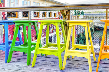 Colorful vivid chairs painted green, yellow and orange on waterfront bar restaurant