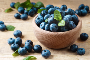 Freshly picked juicy blueberries, green mint leaves in light wooden bowl on rustic table. Bilberry on horizontal wooden top view background. Healthy eating and antioxidant nutrition concept.
