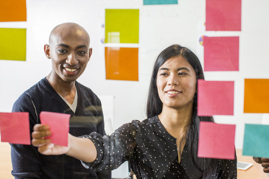 Woman and man reading adhesive notes in office - Powered by Adobe