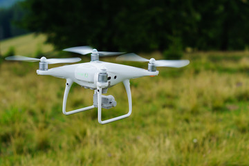 White professional camera drone takes pictures.  Professional copter. Horizontal outdoor background, copy space, selective focus. Quadcopter on green grass.