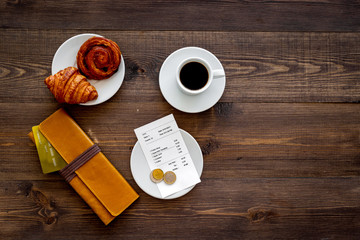 Pay bill at cafe by card. Purse, bill and bank card near coffee and croissant on dark wooden table top view copyspace