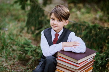 a tired schoolboy sitting on books in park near school