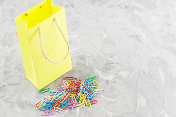 Heap of colored paper clips and one yellow paper bag on old gray cement