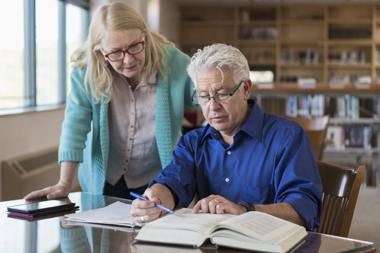 Older woman helping man reading book in library