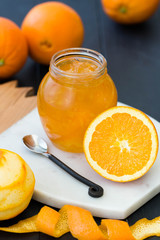 Jar filled with orange jam on the wooden background. Orange marmalade with oranges. Peeled orange. Rustic spoon.