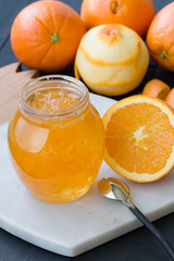 Jar filled with orange jam on the wooden background. Orange marmalade with oranges. Peeled orange.