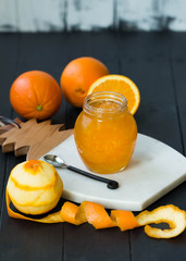 Jar filled with orange jam on the wooden background. Orange marmalade with oranges. Peeled orange. Rustic spoon.
