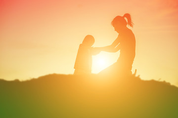 Mother encouraged her daughter out of the shadows at sunset.