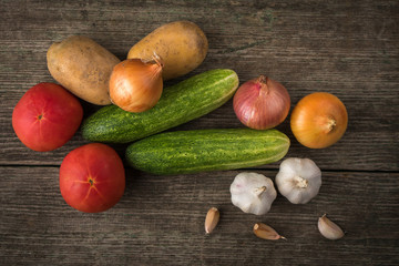 Garlic, onion, cucumber, potatoes and tomato on an old table